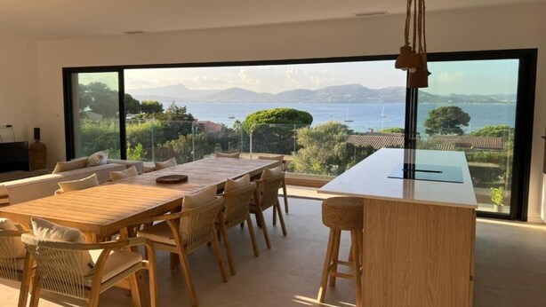 Un espace de restauration moderne avec une table et des chaises en bois, de grandes fenêtres offrant une vue sur la mer et les montagnes.