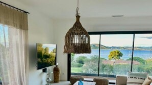 Un salon moderne doté d’une grande fenêtre offrant une vue imprenable sur la mer et la verdure.