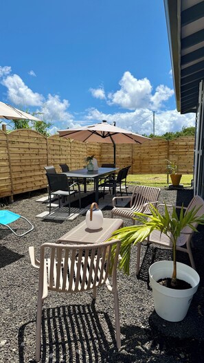 Een terras buiten met een tafel, stoelen, een houten omheining en een bloempot.