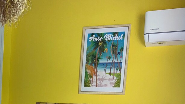 Una camera d'albergo con un letto, cuscini, un comodino con una lampada, un quadro incorniciato al muro e un condizionatore d'aria.