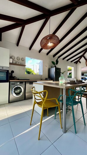 A modern kitchen with a central island, a washing machine, and a dining area with two chairs.