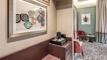 Habitación de hotel con una obra de arte abstracta enmarcada, una mesita con cafetera, una silla roja y una alfombra estampada.