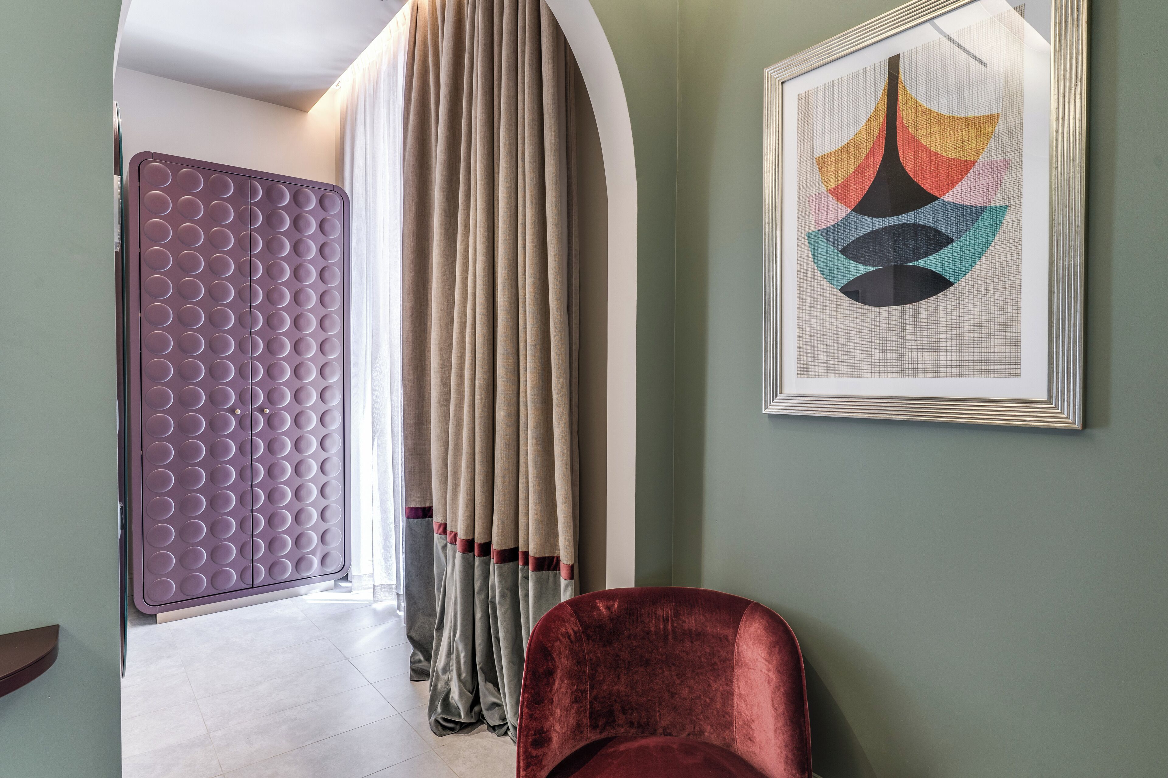 Ein Zimmer mit einer violetten strukturierten Trennwand, einem roten Samtstuhl und einem gerahmten abstrakten Kunstwerk an der Wand.