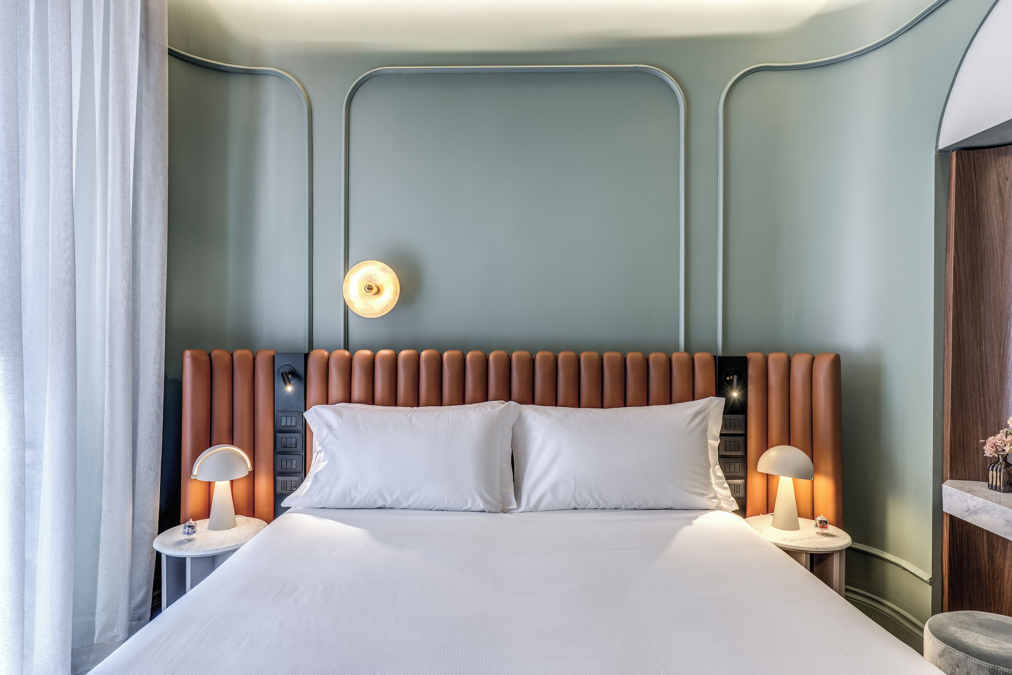 A modern hotel room with a large bed, two bedside tables with lamps, a headboard with vertical panels, and a nightstand with a lamp.