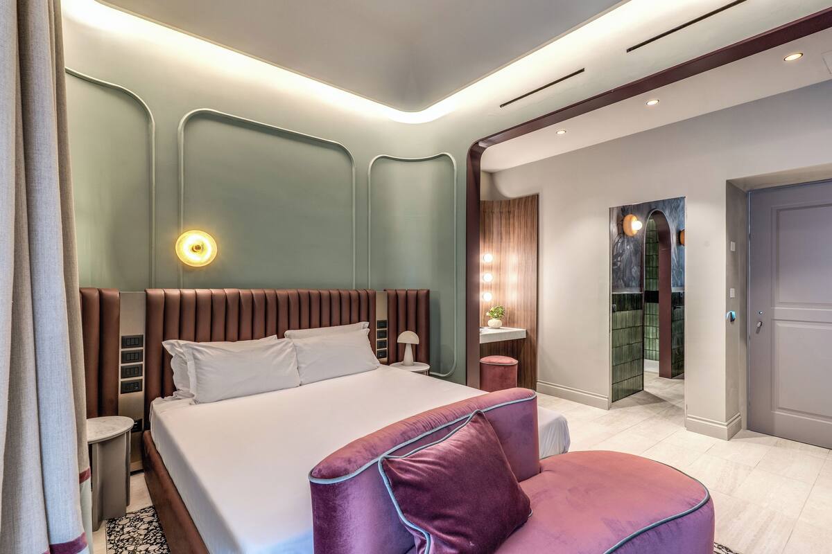 A modern hotel room with a large bed, a seating area, and a vanity with a mirror.