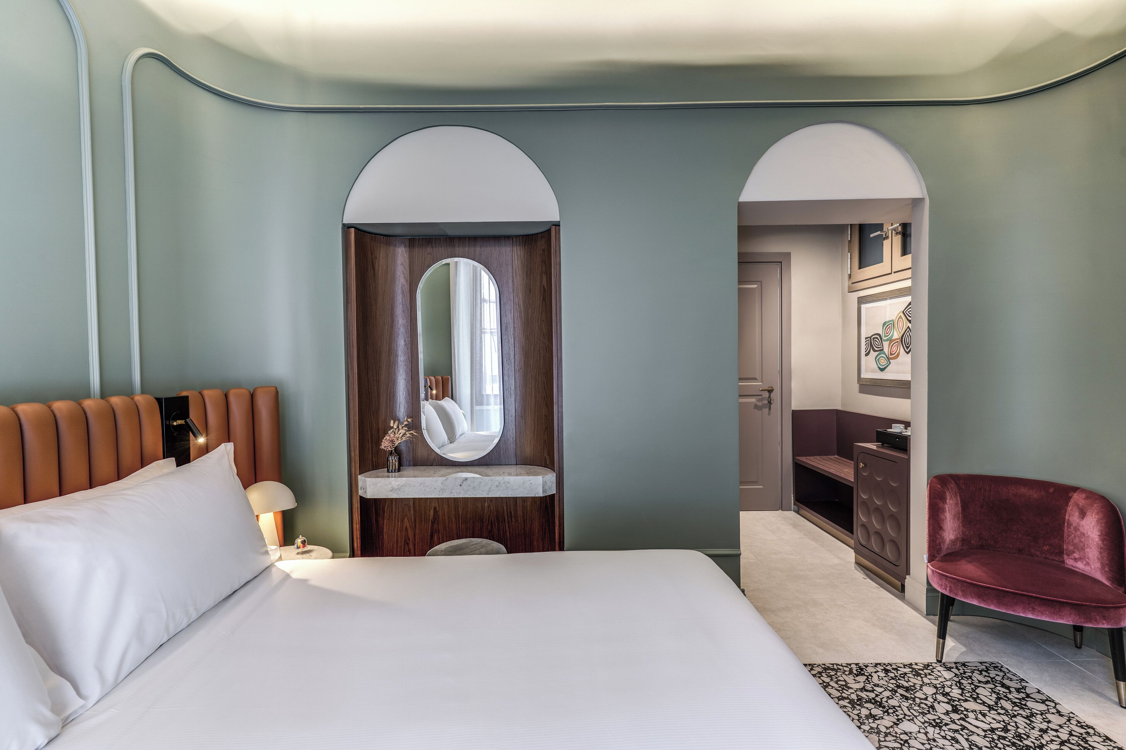 A modern hotel room with a large bed, a vanity with a mirror, a red chair, and a small seating area.