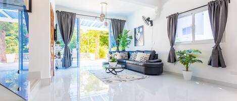 A spacious living room with a black sofa, a coffee table, and a large window with curtains.