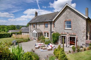 A stone house with a garden patio, a covered outdoor seating area, and a view of the surrounding landscape.