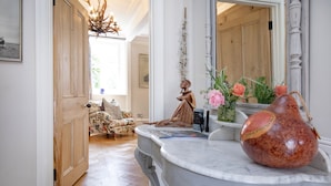 A well-lit hallway with a wooden door, a floral sofa, a marble counter with a vase, and a decorative sculpture. - Linscott Farmhouse in Moretonhampstead (Newton Abbot)