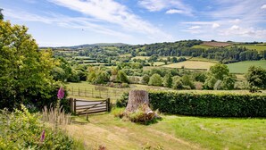 A rural landscape with rolling hills, a wooden fence, and a tree stump. - Linscott Farmhouse in Moretonhampstead (Newton Abbot)