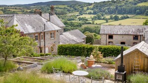 A rustic stone building with a garden and a view of rolling hills. - Linscott Farmhouse in Moretonhampstead (Newton Abbot)