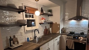 Una cocina con un lavamanos de acero inoxidable, armarios blancos, encimera de madera, estufa y ventana con vistas.