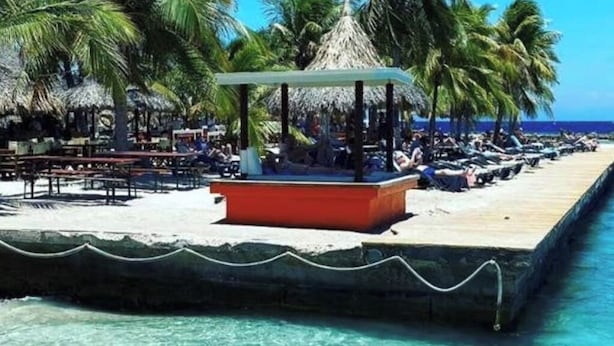 A beachside resort with a thatched-roof gazebo, lounge chairs, and a wooden pier extending into the turquoise sea. - Detached Villa with private pool within walking distance to the beach & restaurants (Jan Thiel)