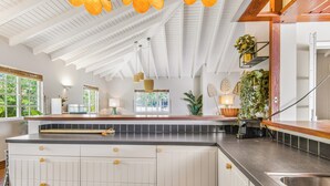A kitchen with white cabinetry, a black countertop, and a large island. There are hanging lights, a window with a view of greenery, and a plant on the countertop. - Detached Villa with private pool within walking distance to the beach & restaurants (Jan Thiel)