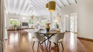 A spacious living area with a round dining table, white chairs, and hanging pendant lights. - Detached Villa with private pool within walking distance to the beach & restaurants (Jan Thiel)