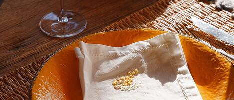 A table with a clear glass wine glass, a green ceramic bowl, and an orange plate with a folded napkin.