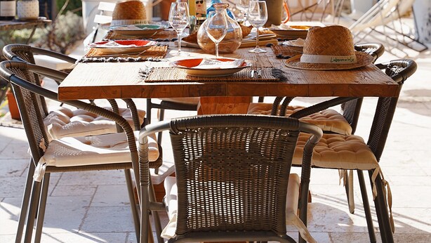 Un espace extérieur aménagé pour les repas, avec des chaises en osier, une table en bois dressée pour un repas, et un luminaire suspendu.