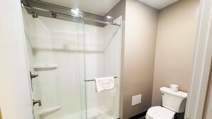 A modern bathroom with a glass-enclosed shower, a toilet, and a small shelf.