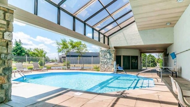 An indoor swimming pool with clear glass ceilings, stone pillars, and a view of the outside.