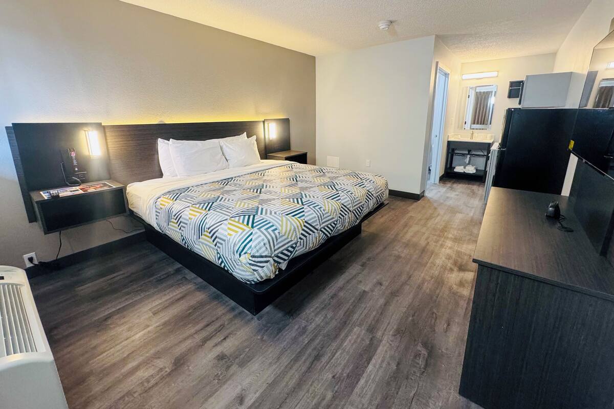 Une chambre d’hôtel moderne avec un grand lit, des tables de chevet, un bureau et une petite kitchenette.