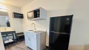 A compact kitchen with a black refrigerator, a built-in oven, a microwave, and a sink.