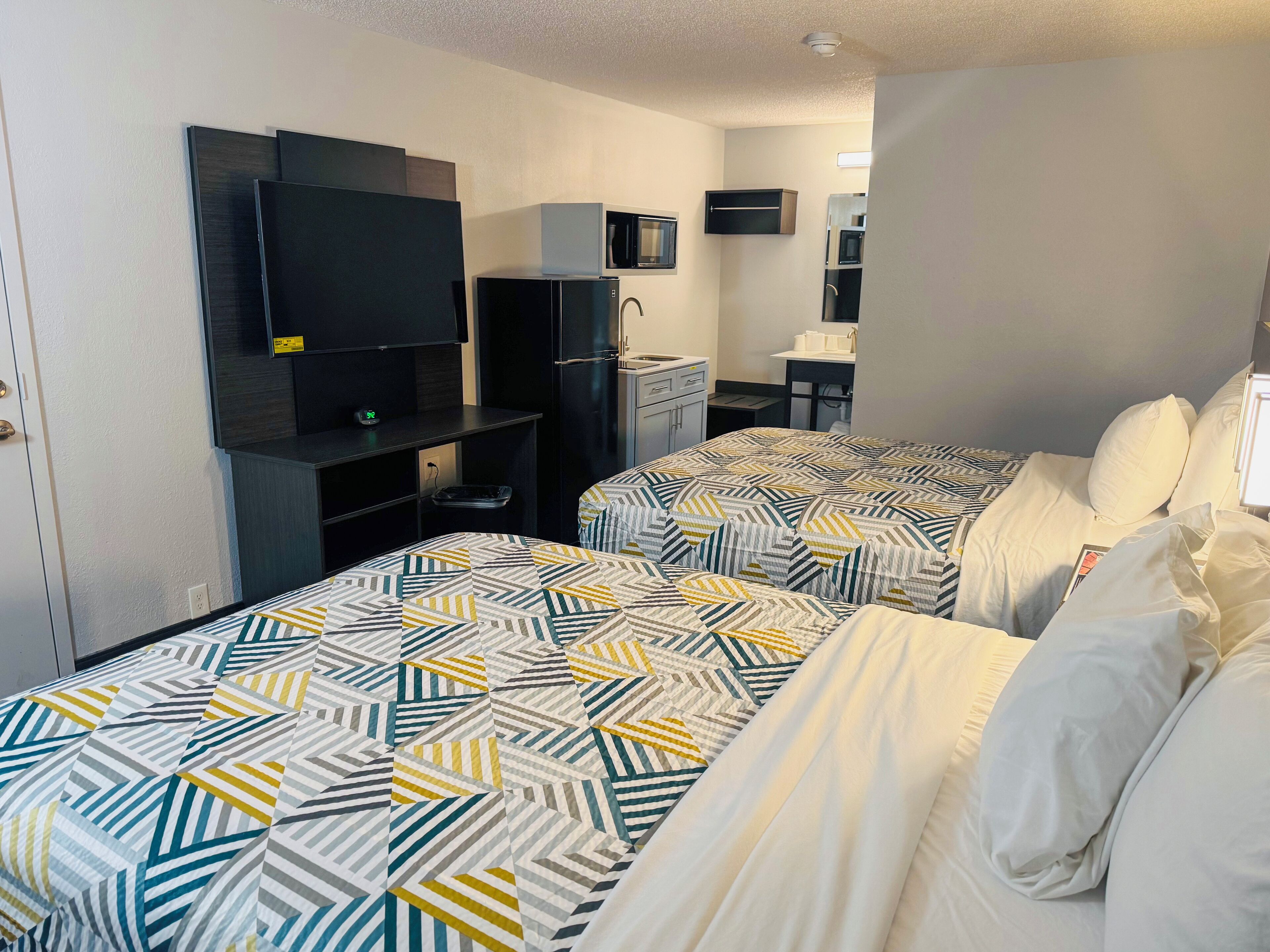 A hotel room with two beds, a TV, a small desk, and a microwave.