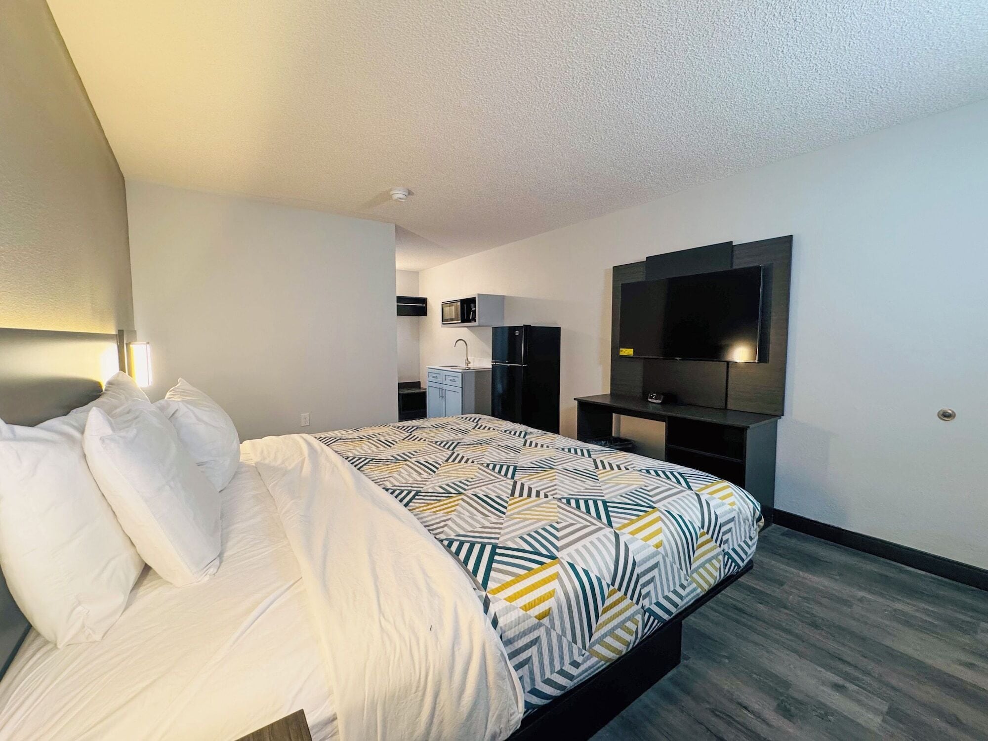 Una habitación de hotel moderna con cama, escritorio, televisor de pantalla plana y kitchenette.