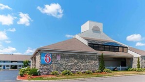 A motel with a stone facade, a large sign with the number 6, and a sloped roof with solar panels.