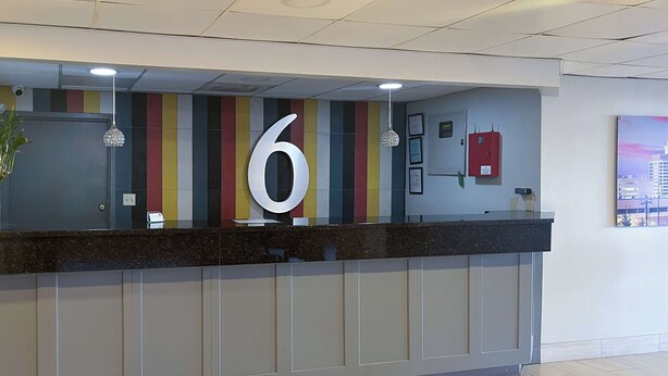 A reception desk with a large number '6' sign, a red fire alarm, and a framed certificate on the wall. - Studio 6 Montgomery, Al – Eastern Blvd. (Montgomery)