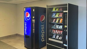 Two vending machines, one for Pepsi and one for Doritos, in a hallway with tiled flooring and a plain wall. - Studio 6 Montgomery, Al – Eastern Blvd. (Montgomery)