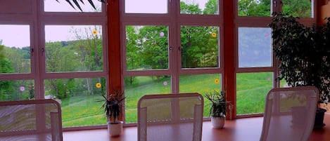 Una habitación con ventanas amplias, sillas blancas y plantas en macetas.