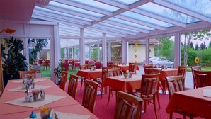 Un restaurante con mesas cubiertas con manteles rojos, dispuestas dentro de una estructura parecida a una tienda con paneles de vidrio.