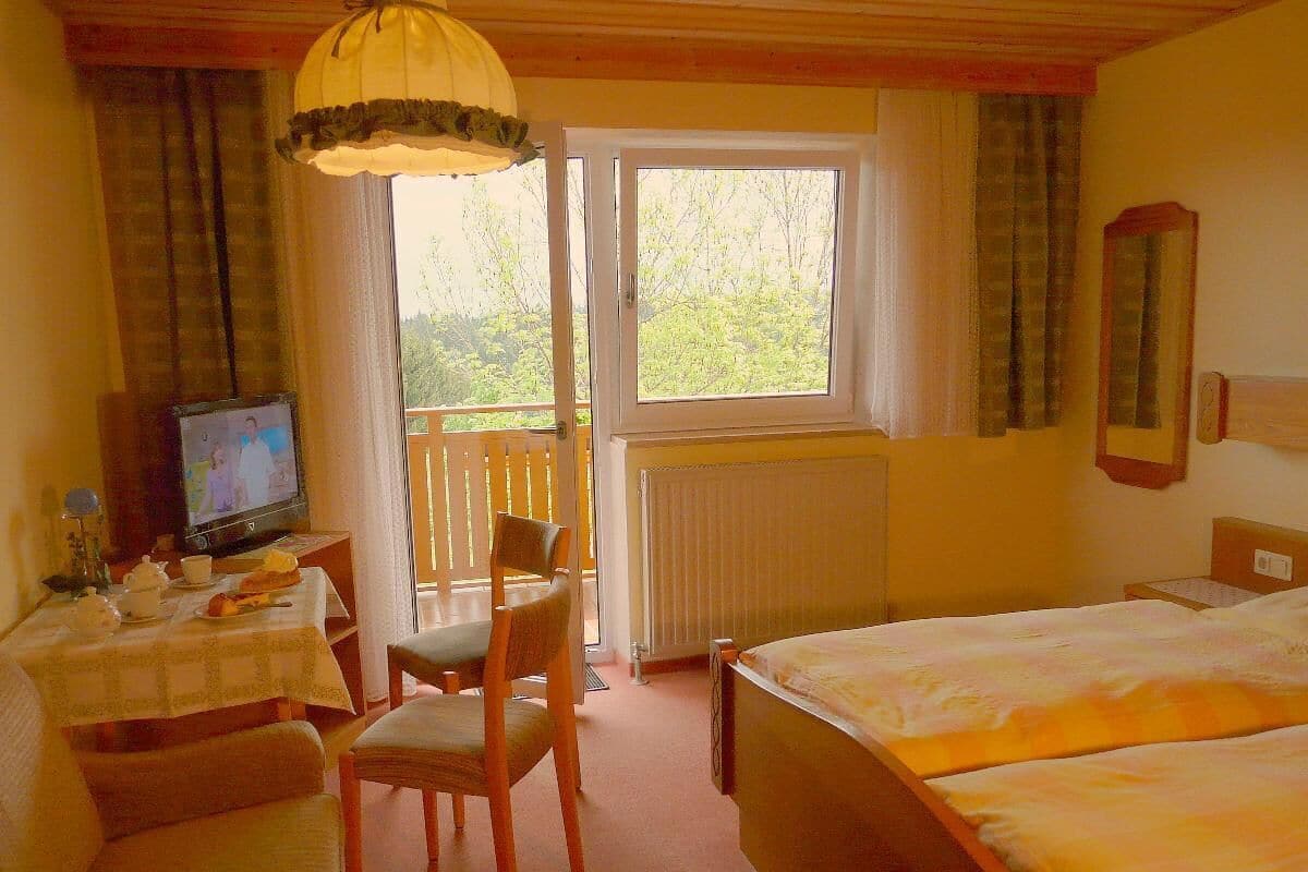 Hotellihuone, jossa on sänky, pöytä ja tuoli, televisio sekä ikkuna, jossa on verhot.