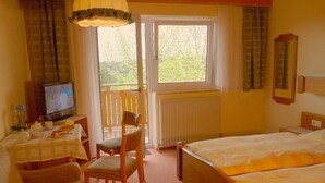 Habitación de hotel con cama, mesa con silla, televisión y ventana con cortinas.