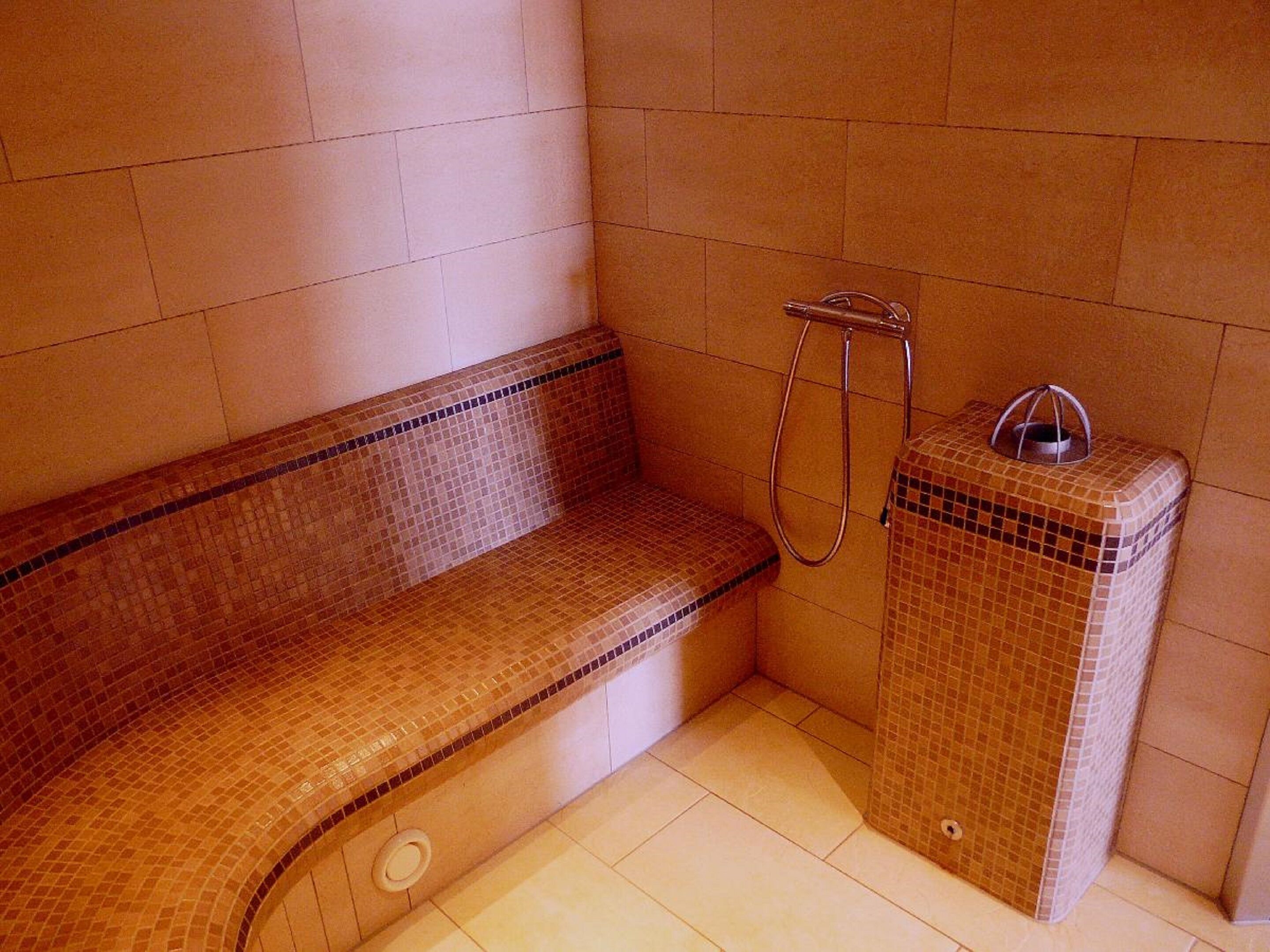 A small, tiled bathroom with a bench and a shower area.