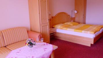 A hotel room with a bed, a sofa, a table with a vase of flowers, and a wardrobe.
