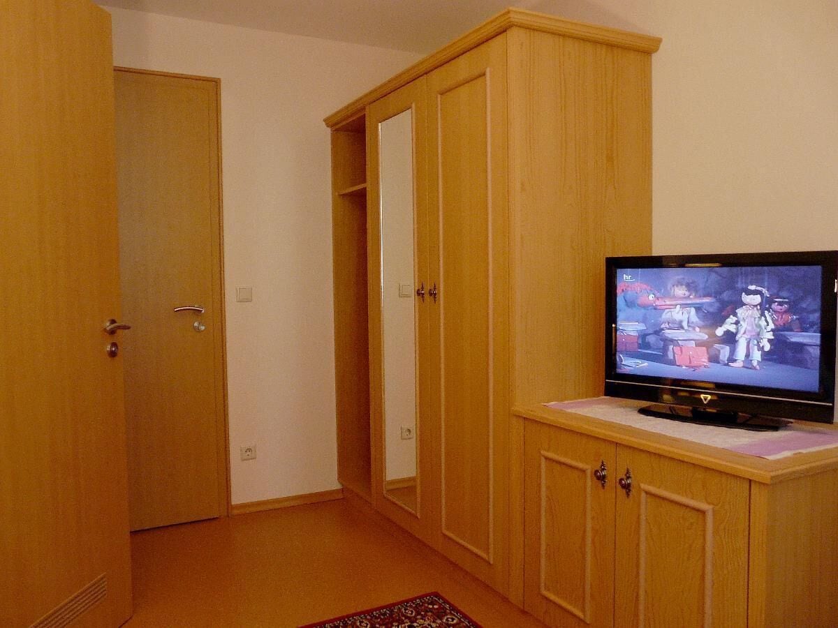 Ein Zimmer mit Holzschränken, einem Fernseher auf einem Schrank und einem gemusterten Teppich.