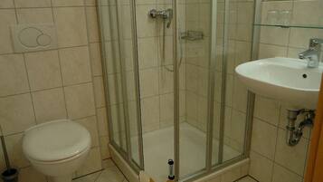 Un baño con inodoro, ducha con mampara de vidrio y lavamanos.