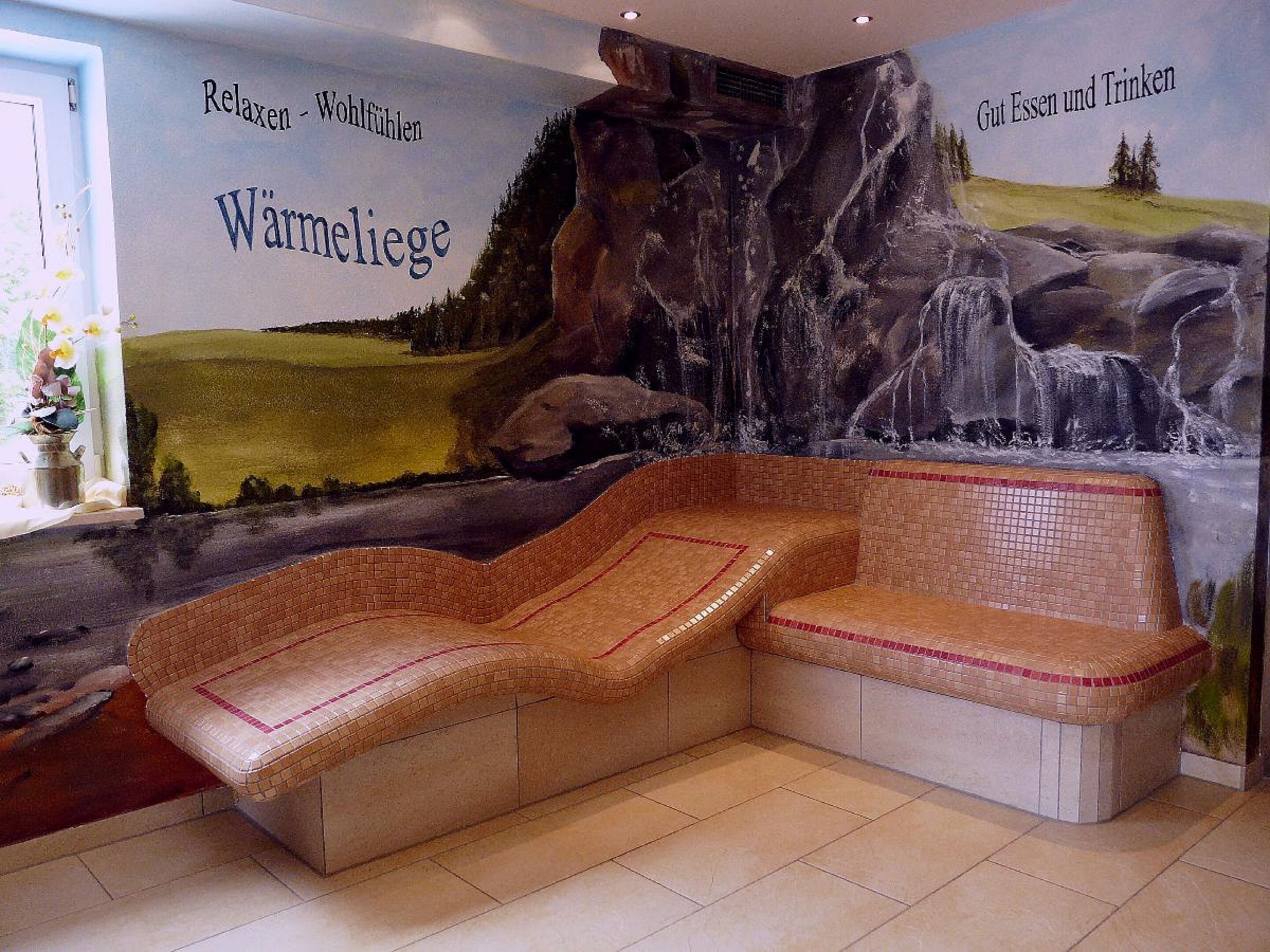 A room with a mosaic bench, a mural depicting a landscape, and text in German on the walls.