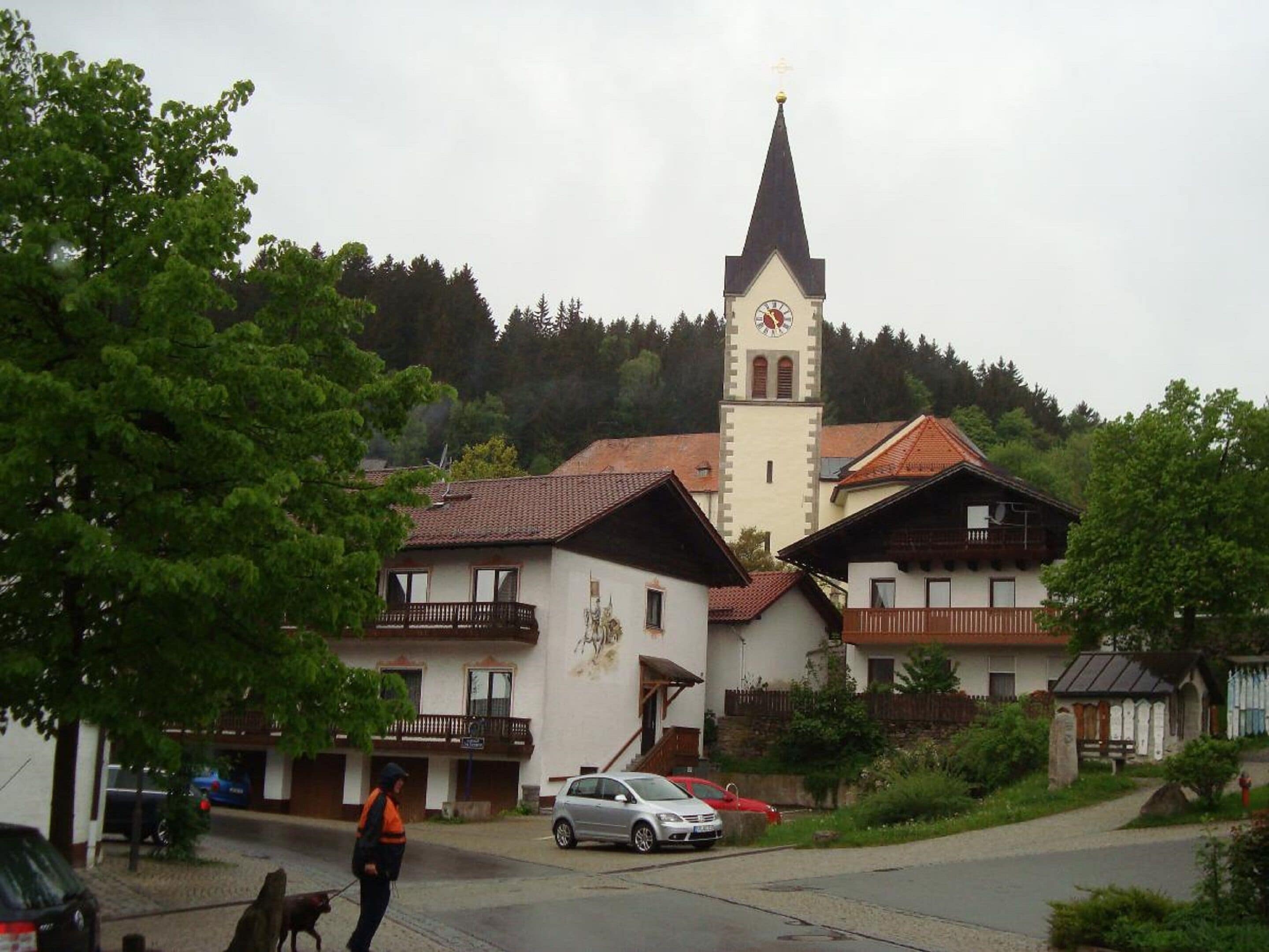 A church with a tall steeple and a clock, surrounded by traditional houses with balconies.
