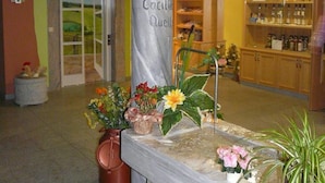 Un área de recepción con una columna de mármol marcada como “Cocitelle Quell”, una puerta de vidrio que da al exterior y un mueble de madera con botellas.
