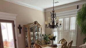 Une salle à manger avec une table en bois, des chaises, un lustre, un buffet aux portes vitrées et une plante en pot.