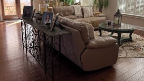 Un salon spacieux avec un canapé en cuir marron, une table basse en verre et un lustre.