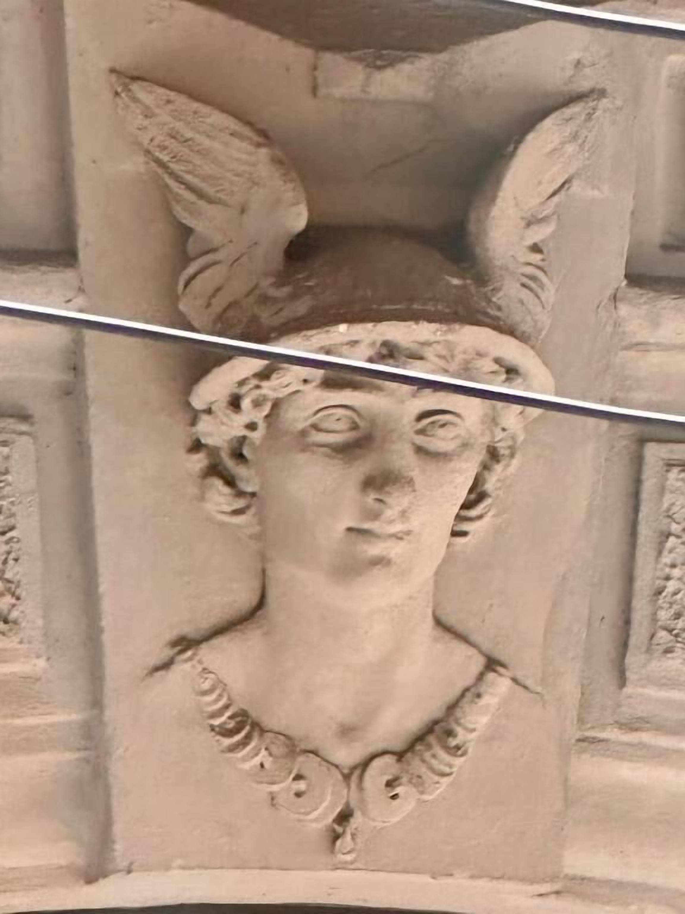 Eine Steinschnitzerei einer Figur mit Flügeln und einer Halskette.