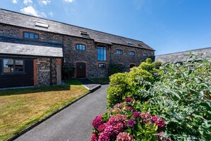 Ein Steinhaus mit befestigter Auffahrt und einem gepflegten Garten mit blühenden Pflanzen.