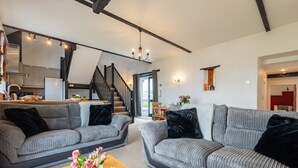 Een moderne woonkamer met grijze banken, een houten salontafel en een trap naar een hoger gelegen verdieping.