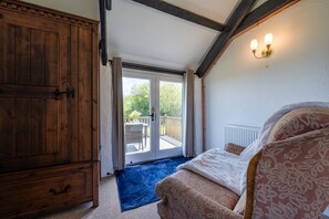 Un dormitorio con un armario de madera grande, una cama con ropa de cama estampada, una alfombra azul y un balcón con mesa y sillas.