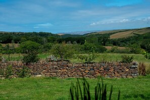 Un mur de pierres dans un champ herbeux, avec des collines qui se dessinent à l'horizon.
