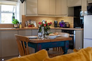Une cuisine avec des meubles de rangement en bois, une table à manger avec des chaises, un vase rempli de fleurs et un grille-pain.
