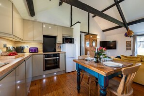 Une cuisine moderne avec un plancher en bois, une table à manger pour deux personnes et un coin salon avec un canapé et un téléviseur.